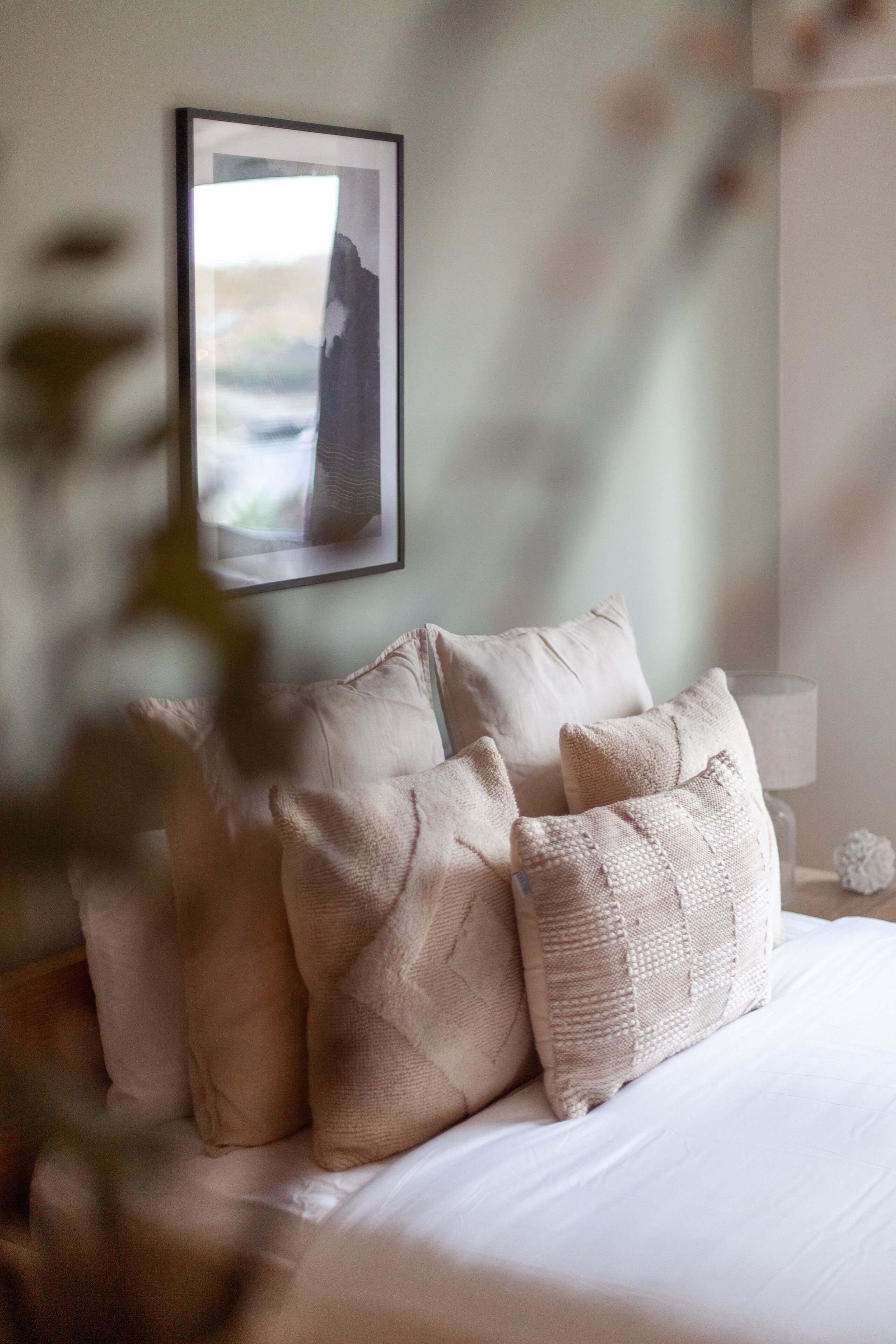 A neatly made bed with multiple pillows, a framed artwork on the wall, and a bedside lamp.