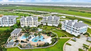 Ein Resort mit mehreren Gebäuden, einem zentralen Poolbereich und Blick auf den Ozean.