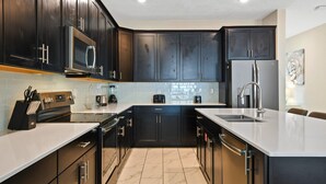 Una cocina moderna con armarios oscuros, un refrigerador de acero inoxidable, un microondas y un fregadero.