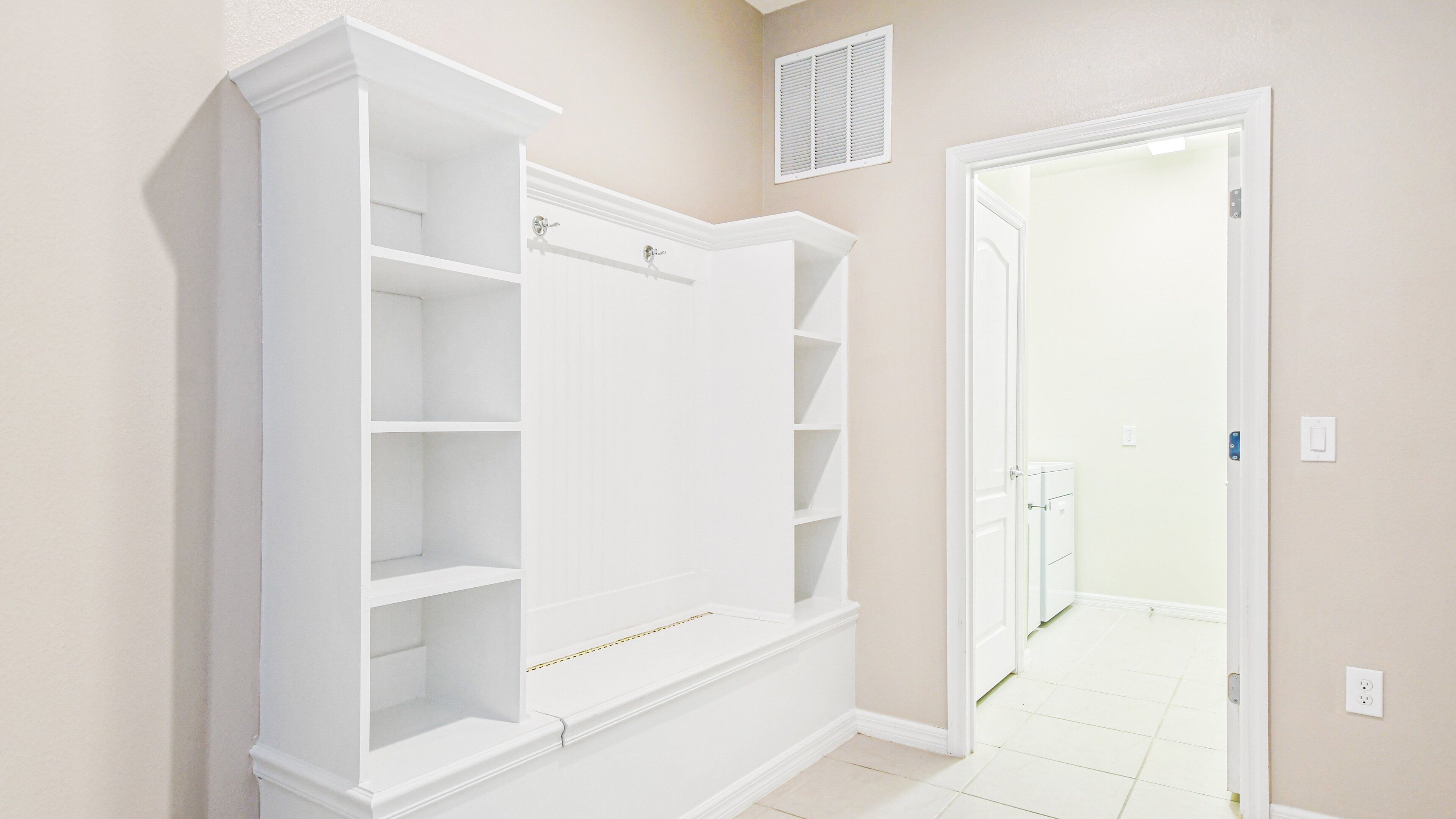 A room with a built-in white shelving unit against the wall, a door leading to another room, and a vent on the wall.