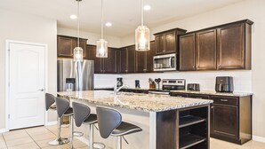 A modern kitchen with dark wood cabinets, stainless steel appliances, a granite countertop, and bar stools.