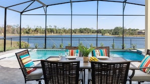 A covered outdoor area with a pool, dining table, chairs, and a view of a lake.