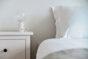 A white bedside table with a clear glass lamp and a white cup. - Il Nido di Maria (Losone)