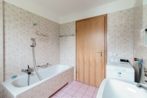 A bathroom with a bathtub, a wooden door, and a washing machine. - Il Nido di Maria (Losone)