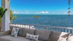 A balcony with a view of the sea, a white railing, and a sofa with decorative pillows.