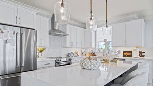 A modern kitchen with white cabinetry, stainless steel appliances, and a marble island.
