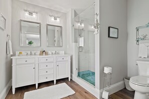 Un baño moderno con un tocador blanco, dos espejos, una ducha con cerramiento de vidrio y un inodoro.