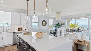 A modern kitchen with a large island, white cabinetry, and pendant lighting.