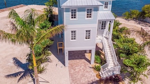 A two-story beachfront house with a covered porch and a staircase leading to the entrance.