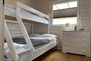 Una cama litera con una ventana arriba, una mesita de noche con una lámpara y un aparador.