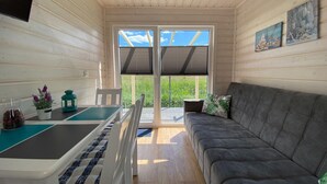 Une pièce chaleureuse avec un canapé, une table à manger et des chaises, et une vue sur la verdure par la porte.