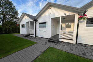 Een wit, twee verdiepingen hoog gebouw met een overdekte veranda, een klein zitgedeelte buiten en een bordje met de tekst 'Beach House'.