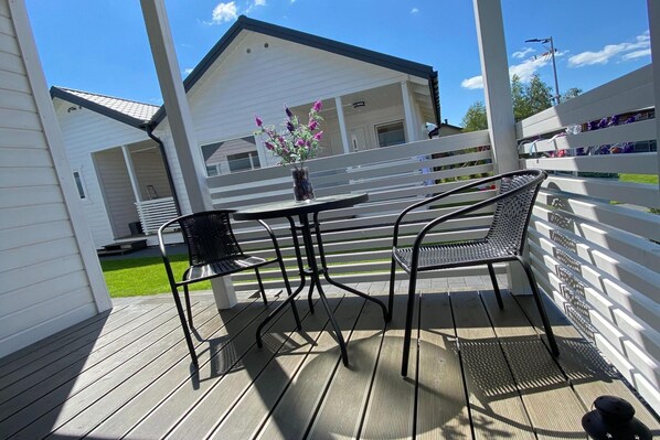 A covered outdoor area with a table and chairs, a white fence, and a building in the background.