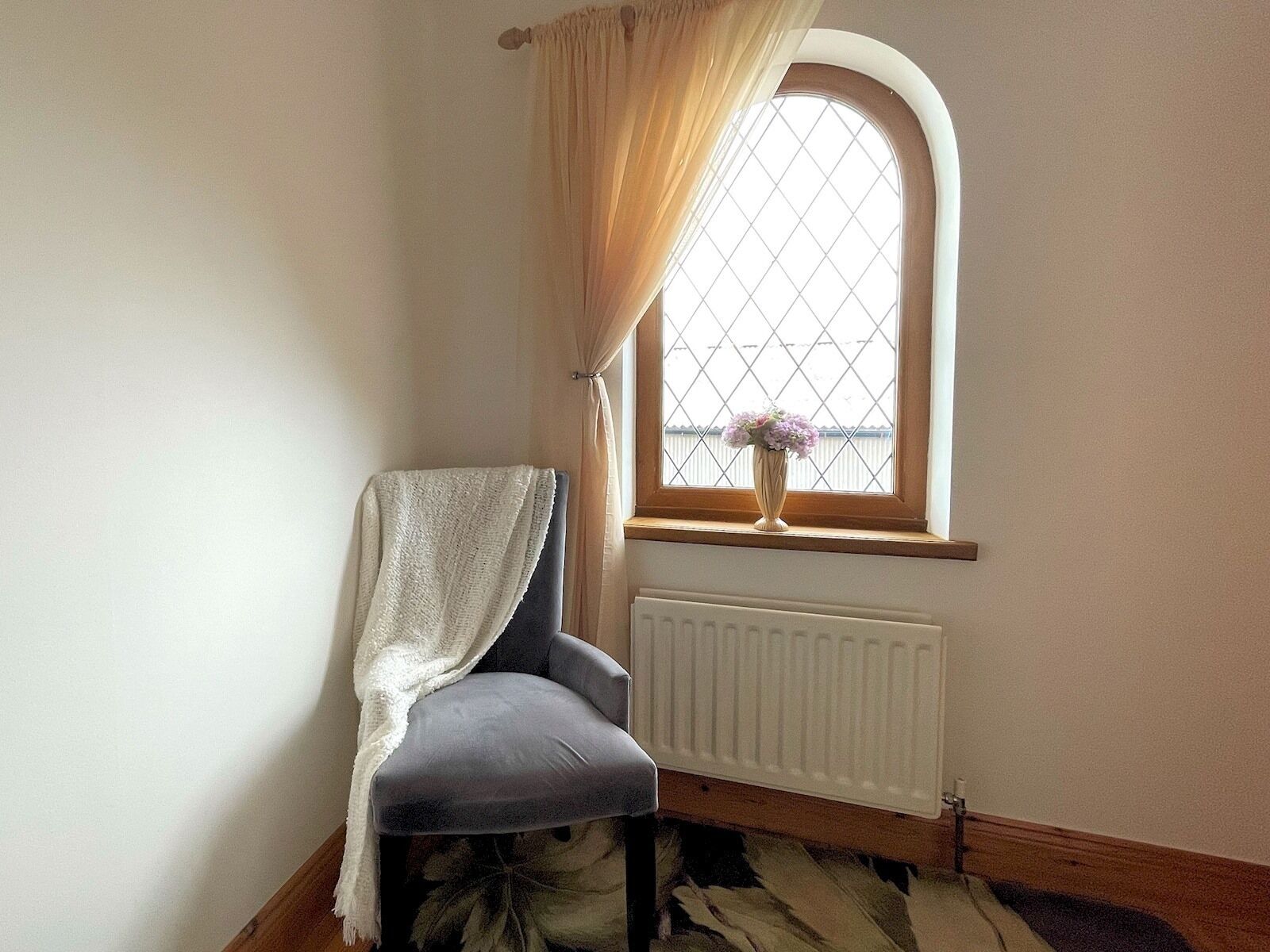 A corner room with a radiator, a window with a curtain, and a chair with a blanket.