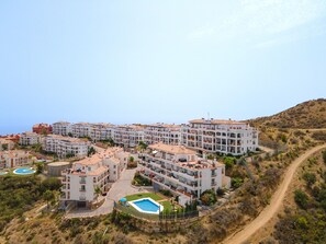 Ett bostadsområde vid kusten med flerfamiljshus, en swimmingpool och en grusväg.