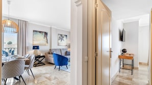 Een moderne woonkamer met een eethoek, een blauwe fauteuil, een bank en een aan de muur bevestigde televisie.
