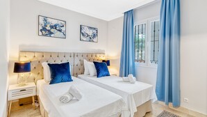 Een hotelkamer met twee bedden, een groot raam met blauwe gordijnen en kunstwerken aan de muur.