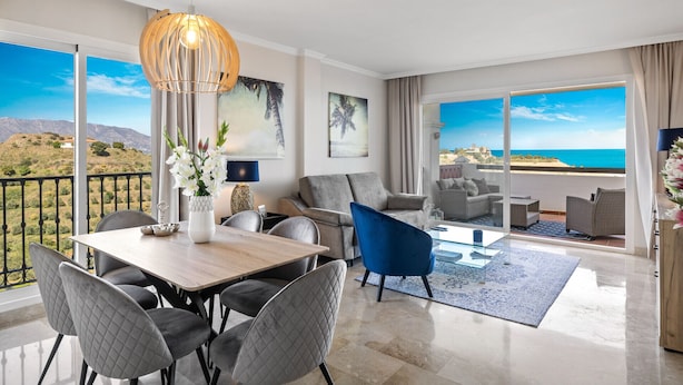 Een moderne woonkamer met een eethoek, grote ramen en uitzicht op zee.