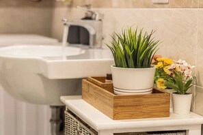 A bathroom with a white sink, a wooden tray with a potted plant and flowers, and a wicker basket. - Dream House With Balcony (Jesi)