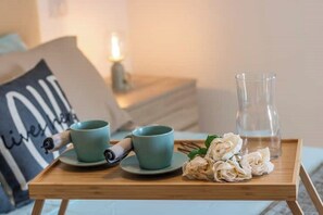A wooden tray with two teal cups, a rolled-up item, and a glass pitcher on a bed with a pillow displaying the word "love". - Dream House With Balcony (Jesi)