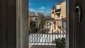 Un balcone con ringhiera in metallo, vista sui palazzi circostanti e cielo sereno.