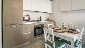 Una cucina moderna con mobili bianchi, forno a incasso, microonde e tavolo da pranzo per quattro persone con sedie bianche.