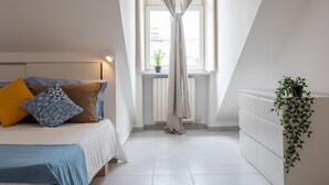 A bedroom with a bed, a window with curtains, a radiator, and a potted plant. - Garibaldi Ten by Wonderful Italy (Turin)