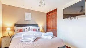 Un letto rifatto con cuscini, una lampada da comodino, una TV a muro e un armadio in legno.