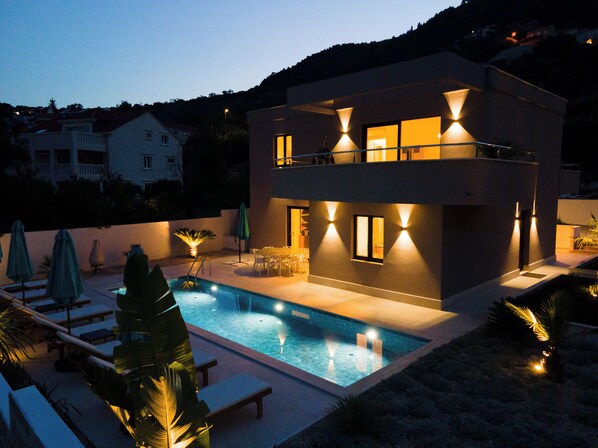 Uma casa moderna de dois andares com piscina, móveis de exterior e vista para o bairro.