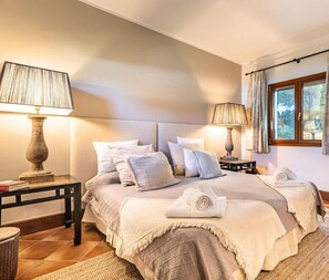 Relax in a serene bedroom with a large bed, two bedside tables, and a window offering a view of lush greenery.