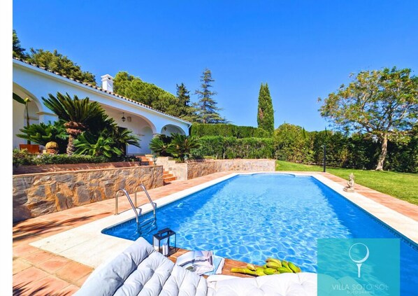 Relax by the serene pool surrounded by lush gardens and a Mediterranean-style building.