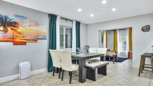 A dining area with a table, chairs, and a painting of a sunset. - Unique Escape GameRoom! Bar, BBQ, Spacious, and Near Beach (Miami)