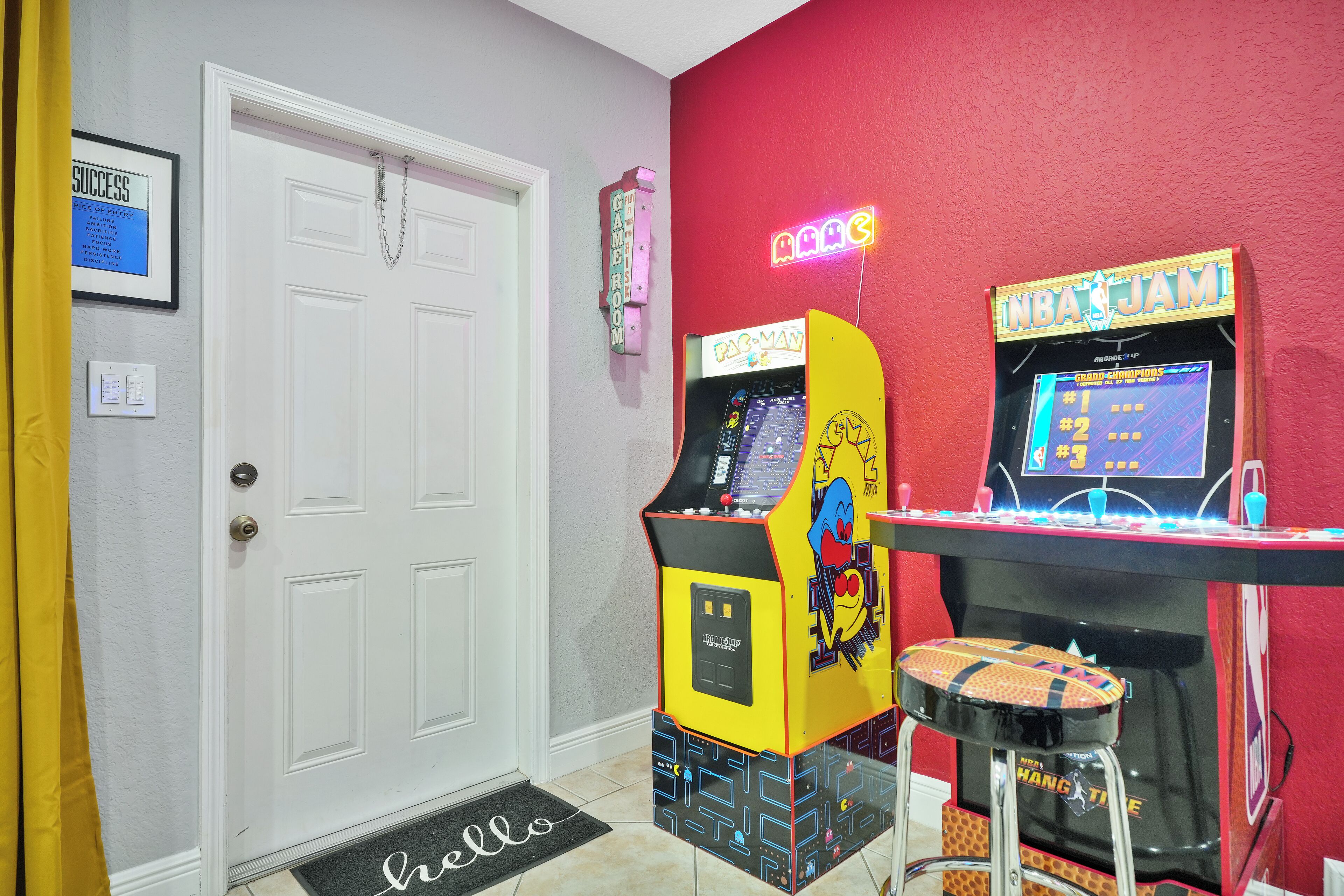 A room with a Pac-Man arcade machine, a Pong machine, and a neon sign.