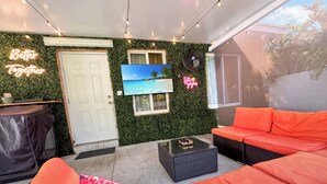 A cozy outdoor seating area with a sofa and a chair, a flat-screen TV mounted on the wall, and a neon sign that reads "Better Together". - Unique Escape GameRoom! Bar, BBQ, Spacious, and Near Beach (Miami)