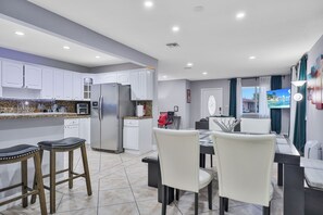 A modern kitchen with white cabinets, a stainless steel refrigerator, and a dining area with a table and chairs. - Unique Escape GameRoom! Bar, BBQ, Spacious, and Near Beach (Miami)
