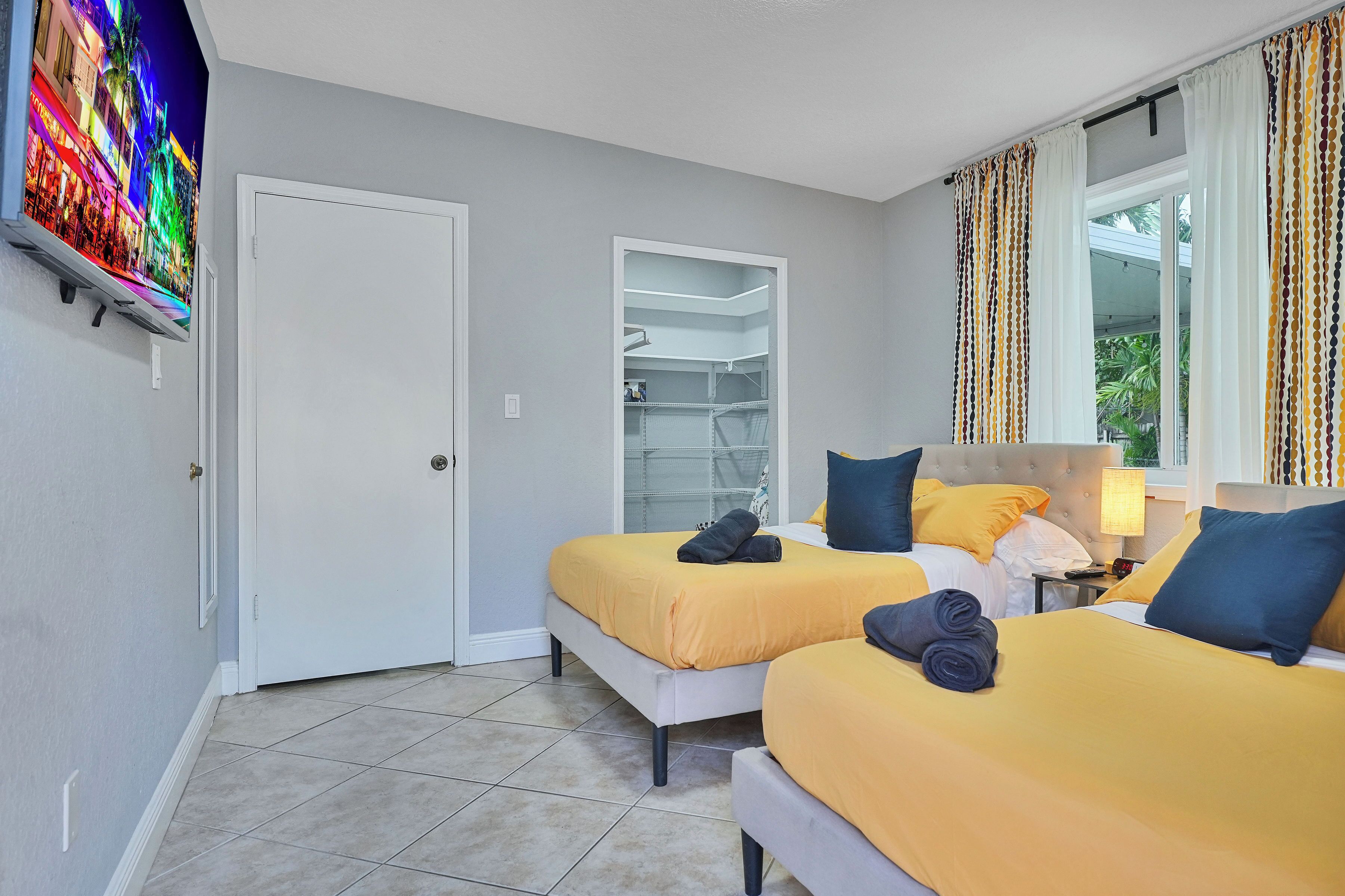 Une chambre d’hôtel avec deux lits, un téléviseur fixé au mur, une armoire et une fenêtre avec des rideaux.