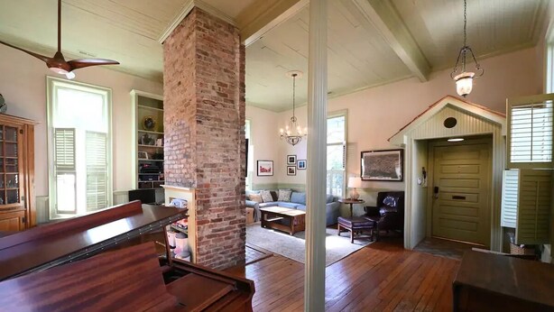 A spacious living room with a grand piano, a brick column, and a cozy seating area with a fireplace.