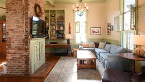 A cozy living room with a brick fireplace, a television, a sofa, and a chandelier.