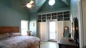 A bedroom with a bed, a ceiling fan, a built-in bookshelf, and a door leading to another room.