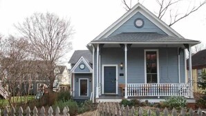 A two-story house with a front porch, a small garden, and a wooden fence.
