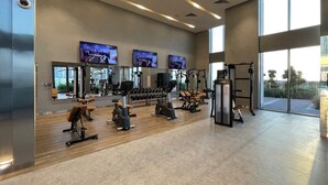 A modern gym with various exercise equipment, large mirrors, and TVs on the walls.