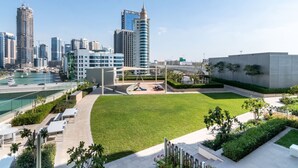 A modern urban area with a large open grassy space, a playground, and a view of the city skyline including high-rise buildings.