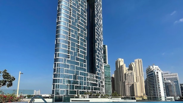 A modern high-rise building with a unique curved design, situated next to a swimming pool with clear blue water.