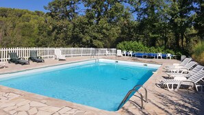 A rectangular swimming pool with a stone tile border, surrounded by white lounge chairs and a white fence.