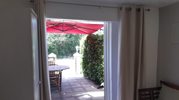 A room with a sliding glass door leading to an outdoor patio area with a red umbrella, a table, and chairs.