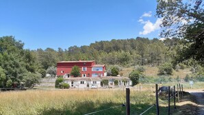 A red two-story house with a tiled roof, surrounded by a fenced field and trees.