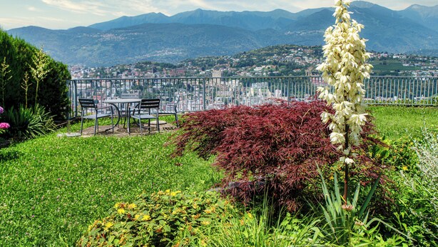A balcony with a city view, a table and chairs, and a variety of plants. - Aldesago City View (Lugano)