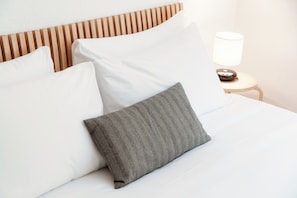 A neatly made bed with white and gray pillows, a wooden headboard, and a bedside table with a lamp. - Aldesago City View (Lugano)