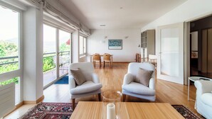 A spacious living room with a large window, a dining area, and a view of greenery. - Aldesago City View (Lugano)