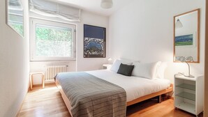 A bedroom with a bed, bedside table, lamp, and a window with a view of trees. - Aldesago City View (Lugano)